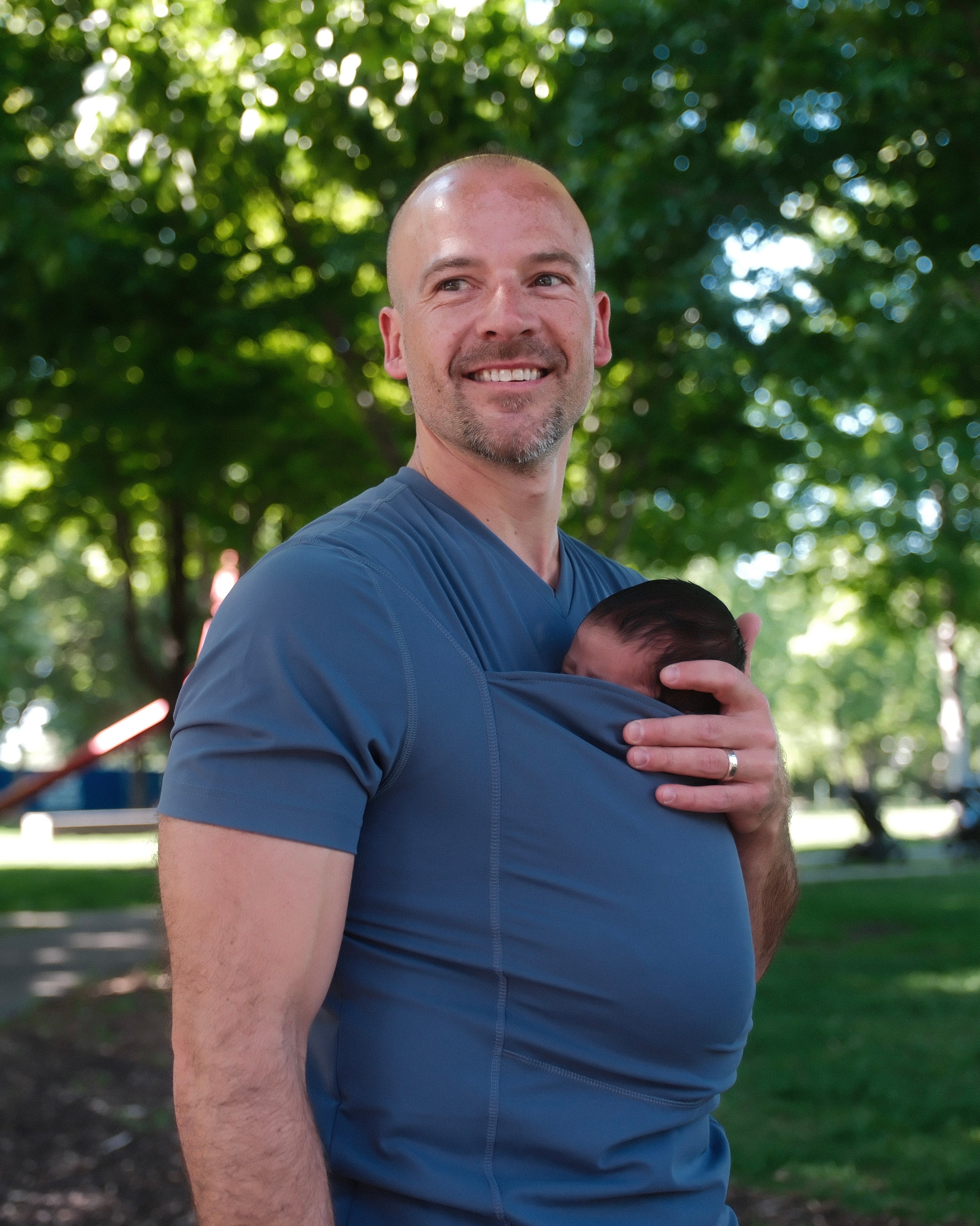 Dad smiling while supporting the head of the newborn in the pouch of his Dad Shirt.