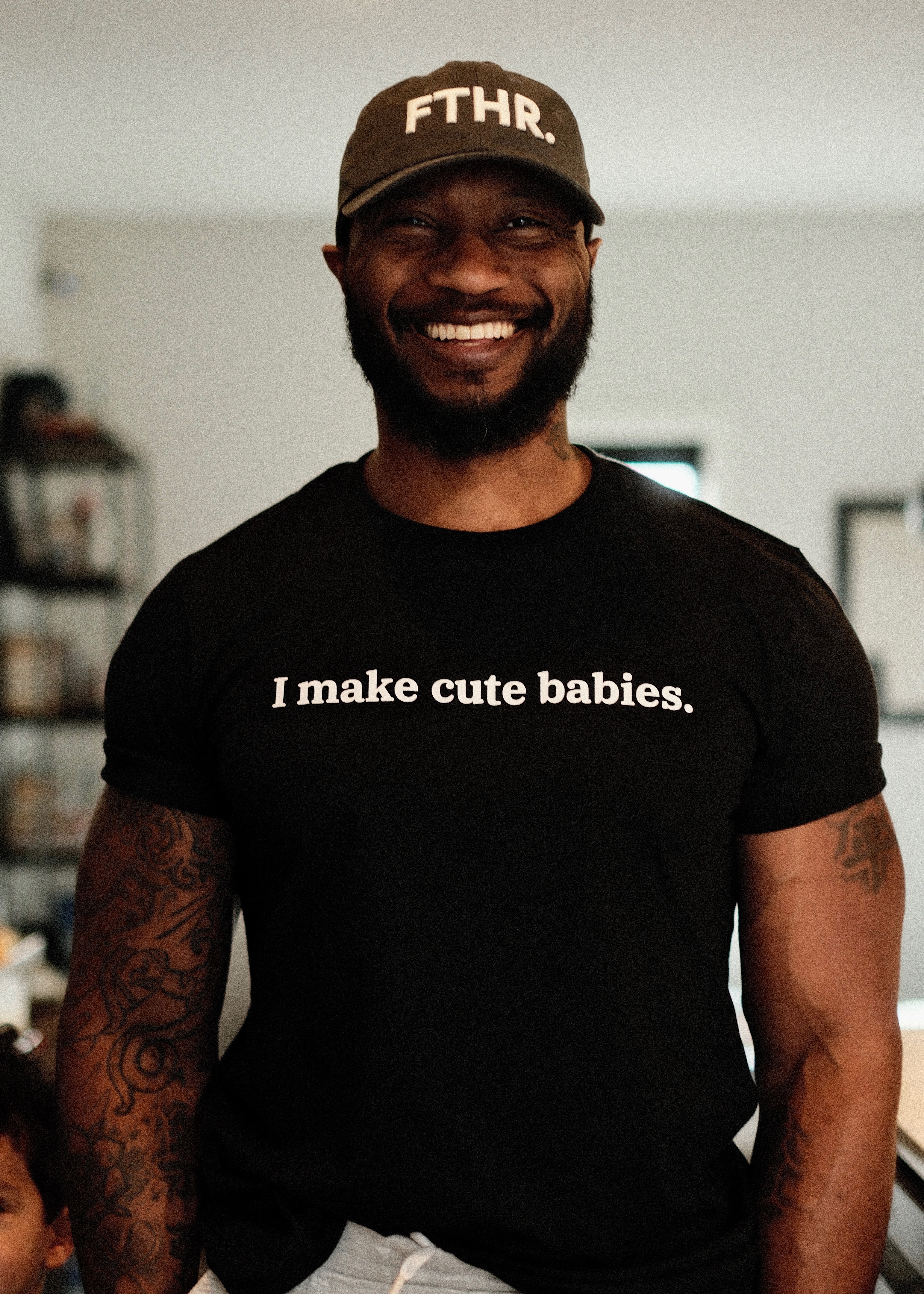 Dad wearing a charcoal cap with 'FTHR.' and a black t-shirt with 'I make cute babies.' text.