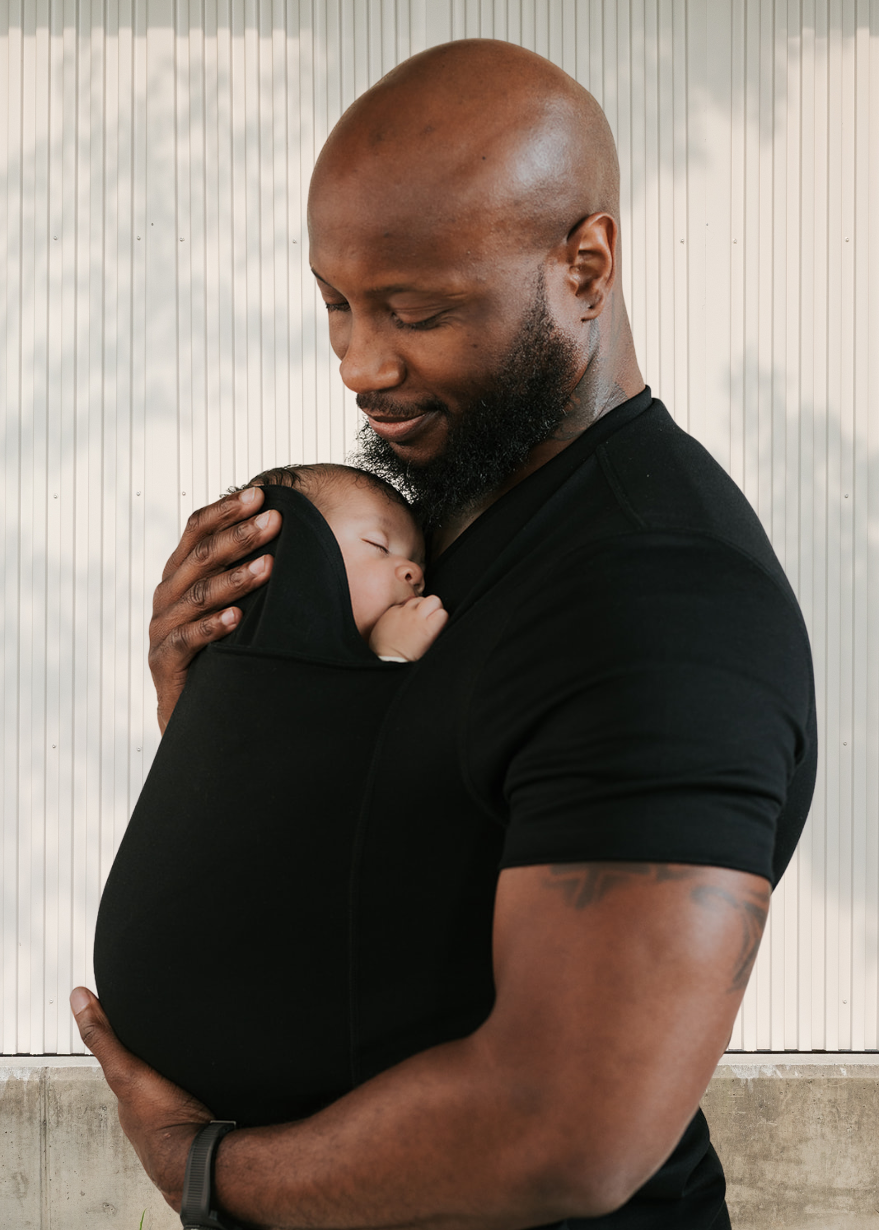 Dad snuggling the newborn in the pouch of his black Dad Shirt.