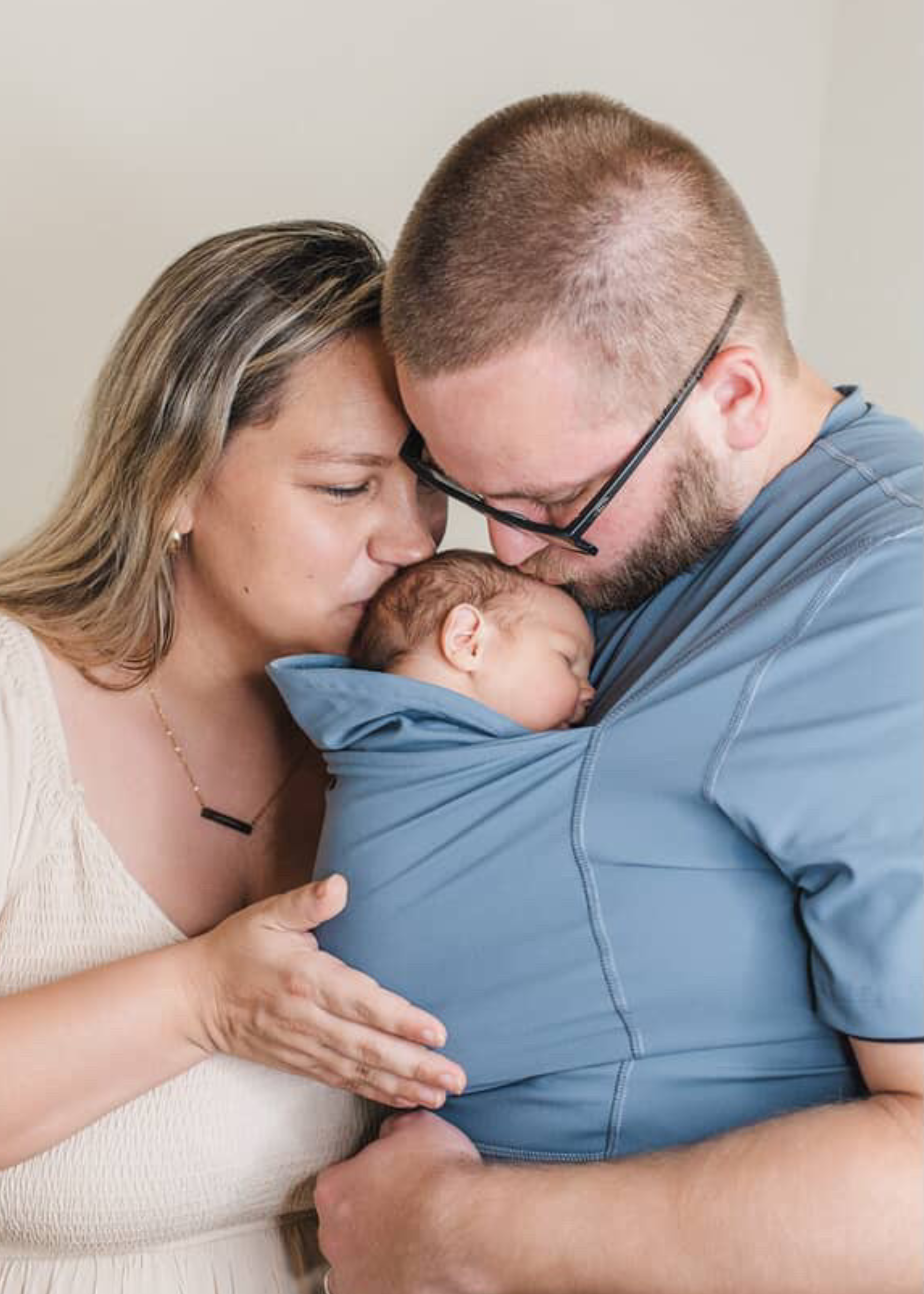 Mom and Dad kiss the head of their baby in the pouch of Dad's Brook Dad Shirt.