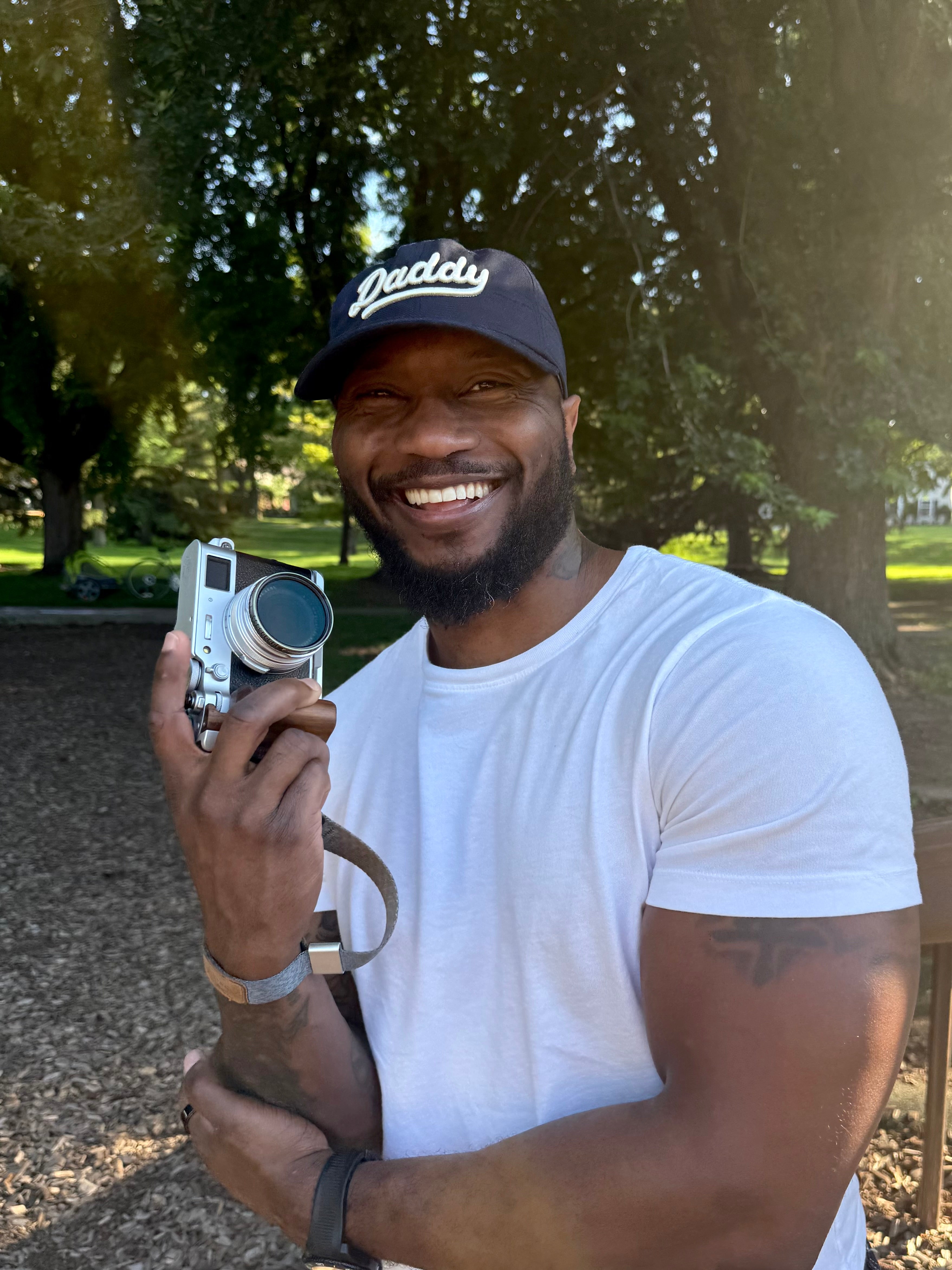 Man wearing the navy "Daddy" hat from Lalabu while holding a camera at a park.