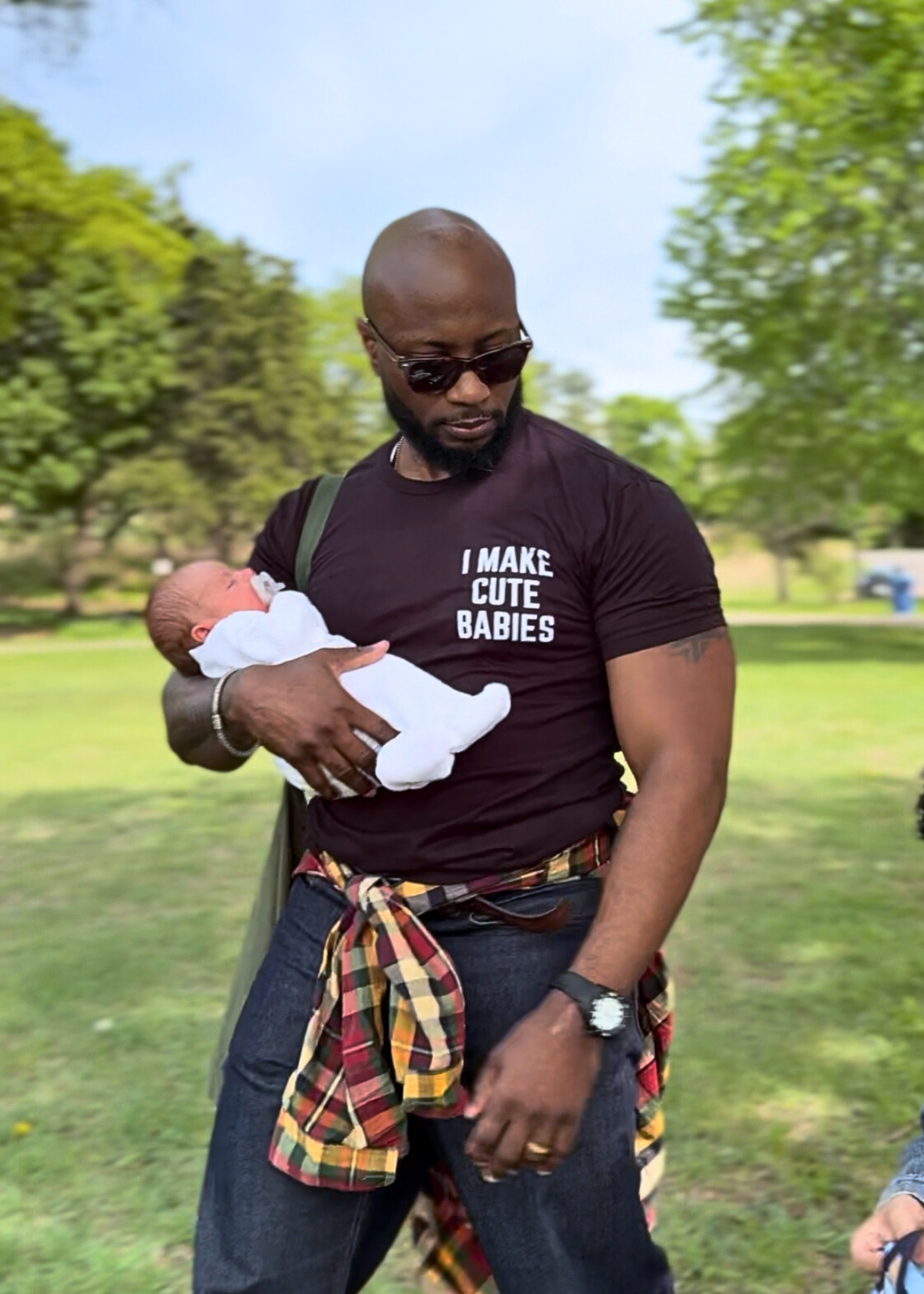 Dad wearing the "I Make Cute Babies" black t-shirt while holding a baby at the park.