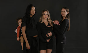 3 females in all black. 1 back carrying a toddler in a Simple Wrap, 2 wearing babies in Soothe Shirts.