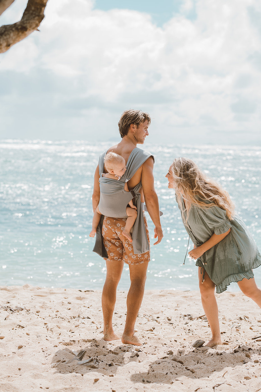 Dad back carrying baby in a simple wrap with mom on the beach.