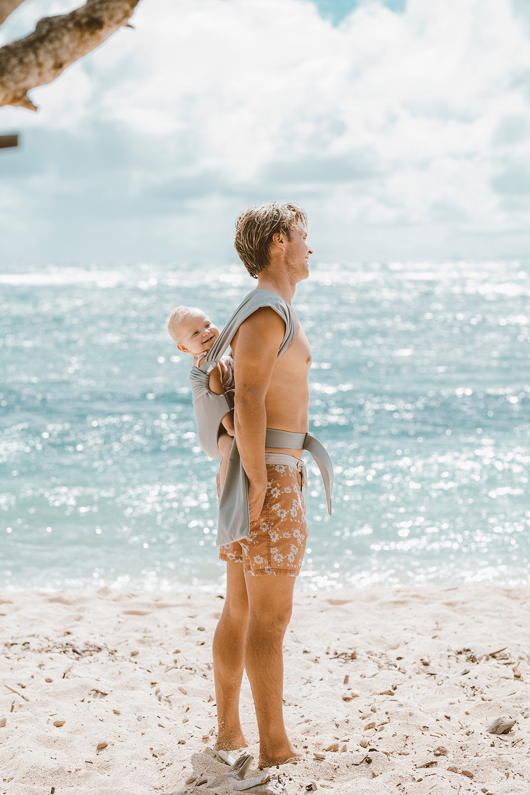 Side view of Dad back carrying baby in a simple wrap on the beach.