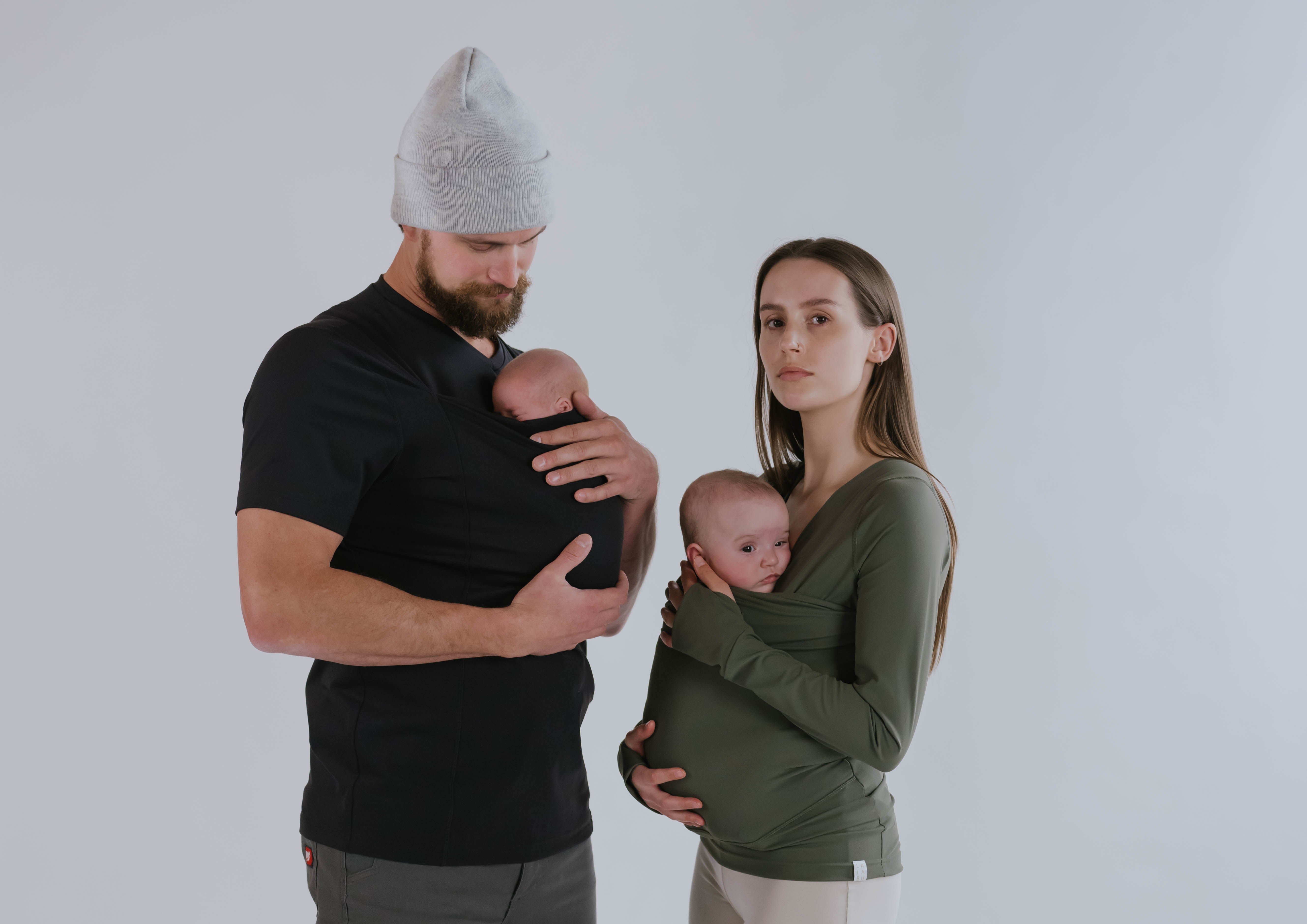 Male wearing a newborn in a black Dad Shirt standing next to a female wearing a newborn in a Fern long sleeve Soothe Shirt.