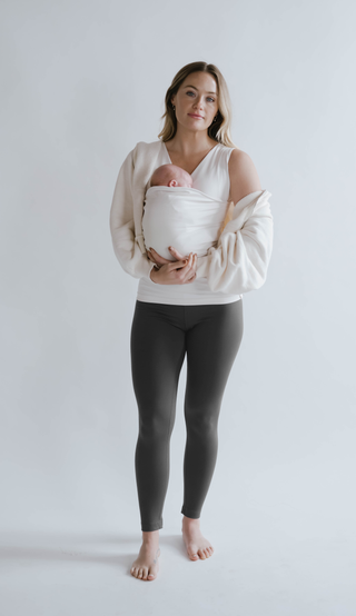 Front view of a female in gray high waisted leggings with a newborn in a Soothe Shirt.