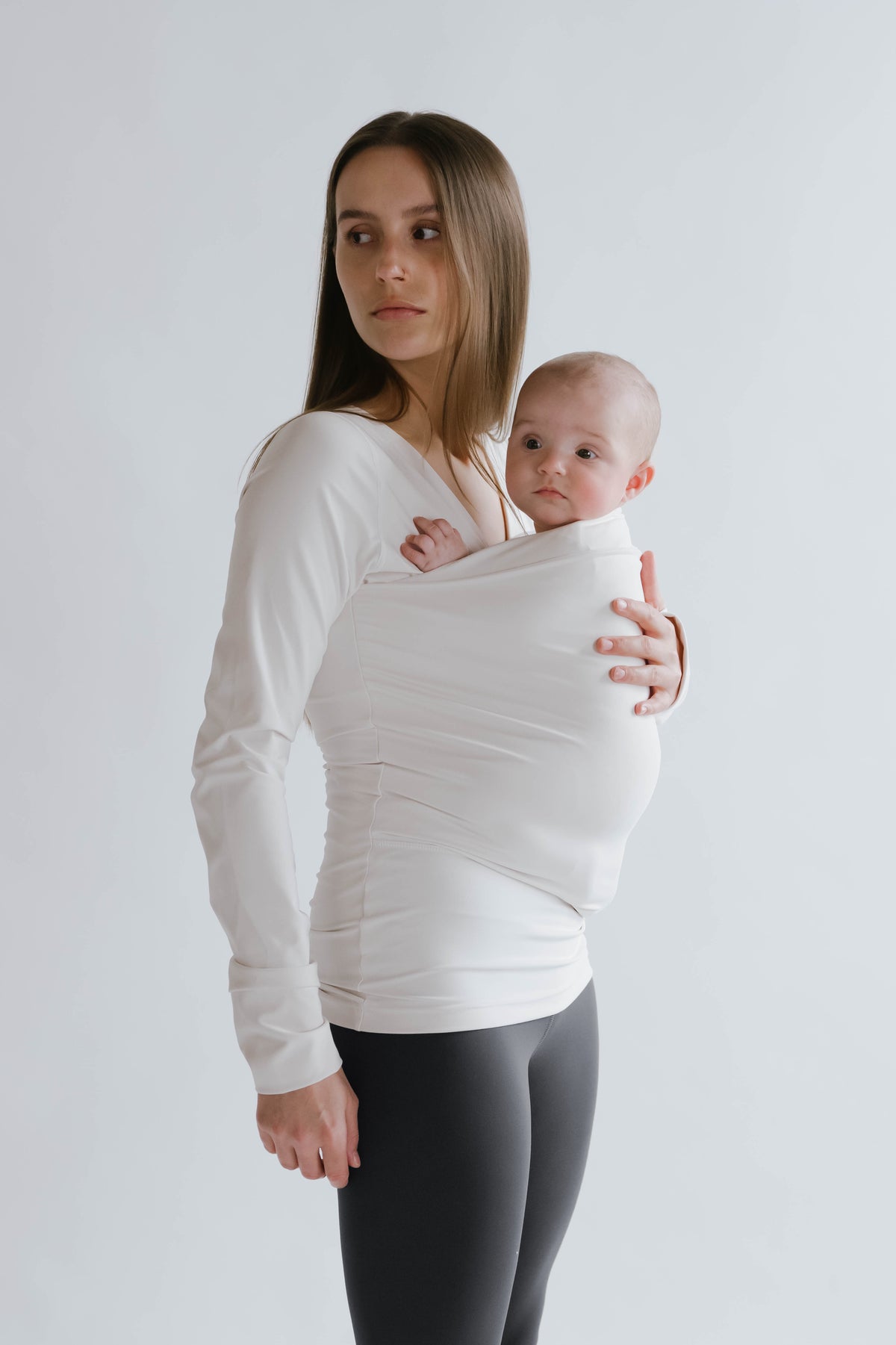 Side view of a female in gray high waisted leggings with a newborn in a long sleeve Soothe Shirt.