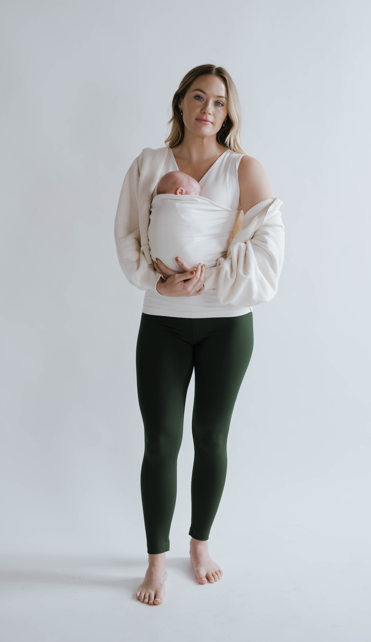 Front view of a female in green high waisted leggings with a newborn in a Soothe Shirt.