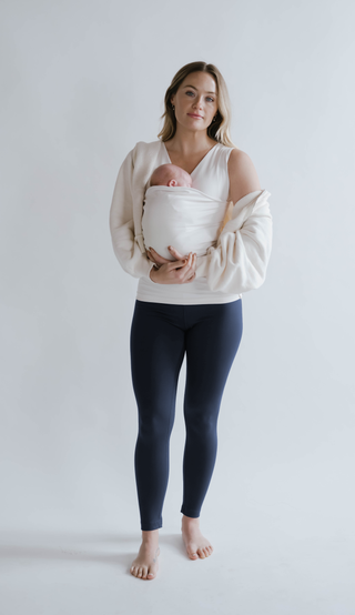 Front view of a female in navy high waisted leggings with a newborn in a Soothe Shirt.