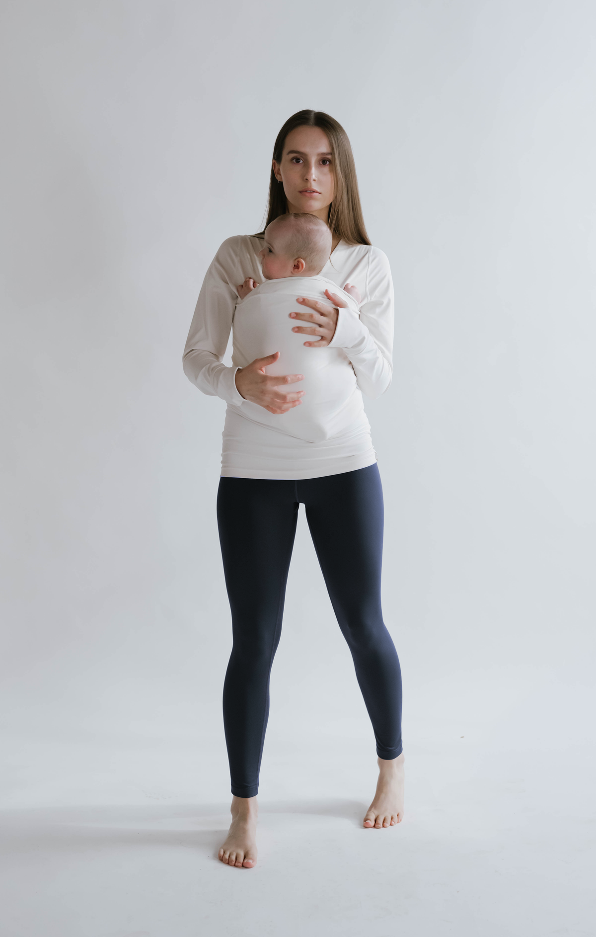 Front view of a female in navy high waisted leggings with a newborn in a long sleeve Soothe Shirt.