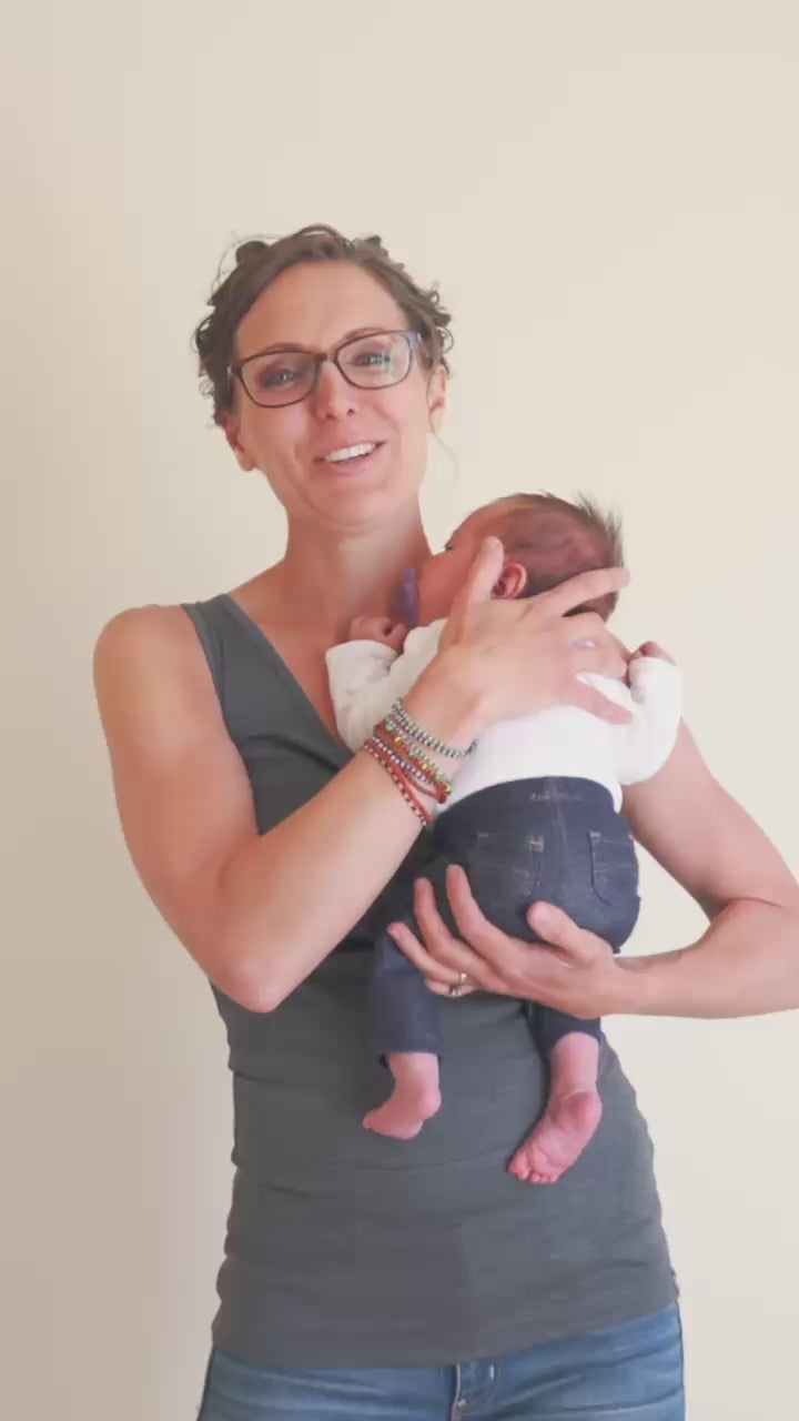 Load video: Mom demonstrating how to use a Soothe Shirt. "You simply scoot the baby up on your shoulder, pull the pouch down around their feet, help them slide in, and pull it up. It's that easy."
