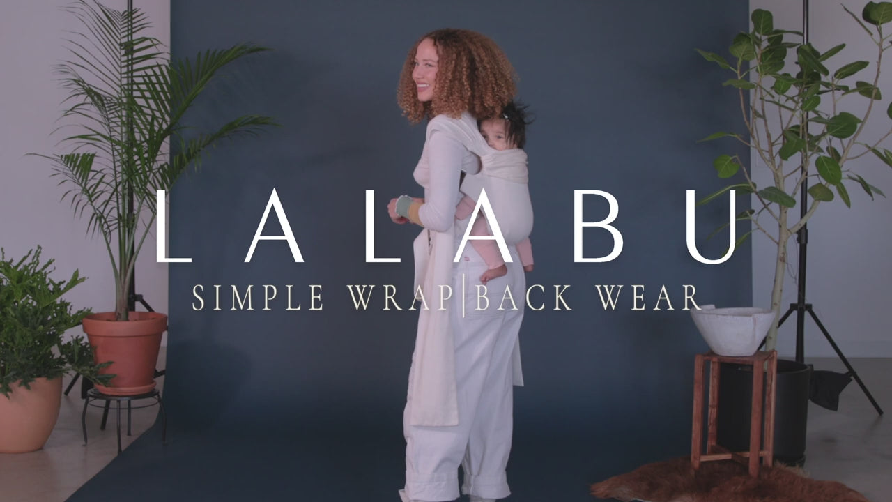 Load video: Lalabu Simple Wrap, back wear. Straps are threaded like a backpack. Waistband is clipped so that the buckle is in the front. Wearer can slide baby to their back or have someone place baby on their back. Place an arm through each carrier to secure baby. Tighten straps as needed.