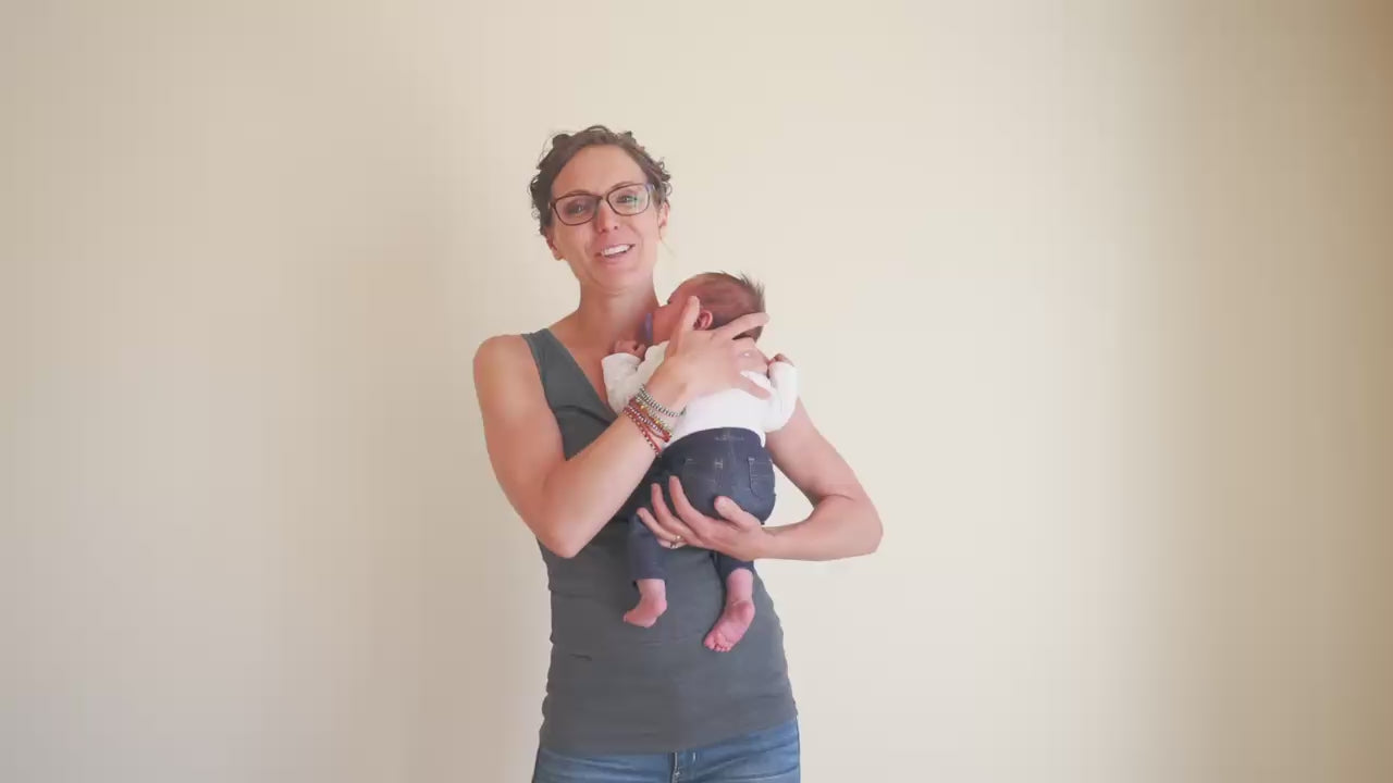 Load video: Mom demonstrating how to use a Soothe Shirt. "You simply scoot the baby up on your shoulder, pull the pouch down around their feet, help them slide in, and pull it up. It's that easy."