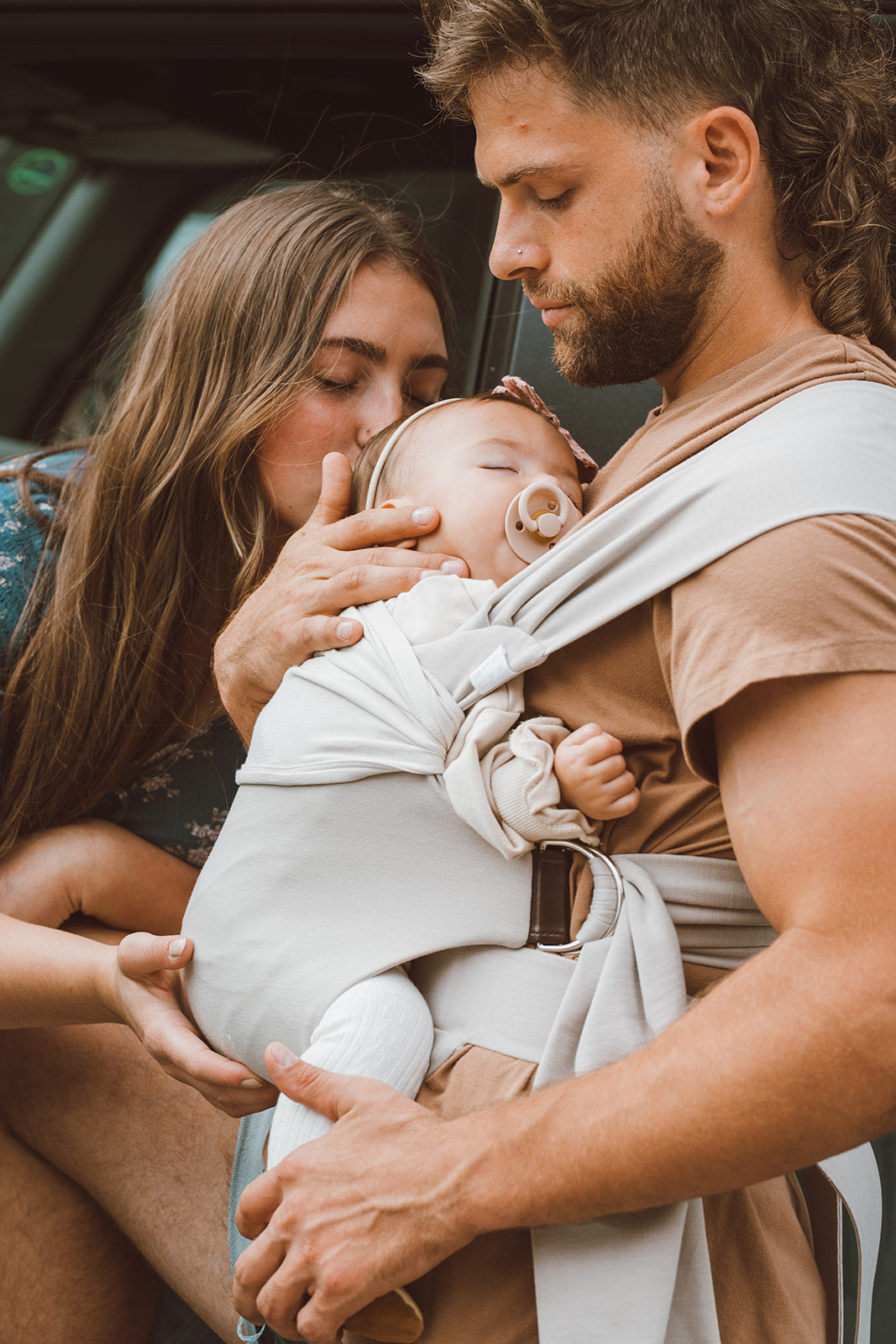 Male front carrying a baby in a Flax Simple Wrap with a female kissing the baby.