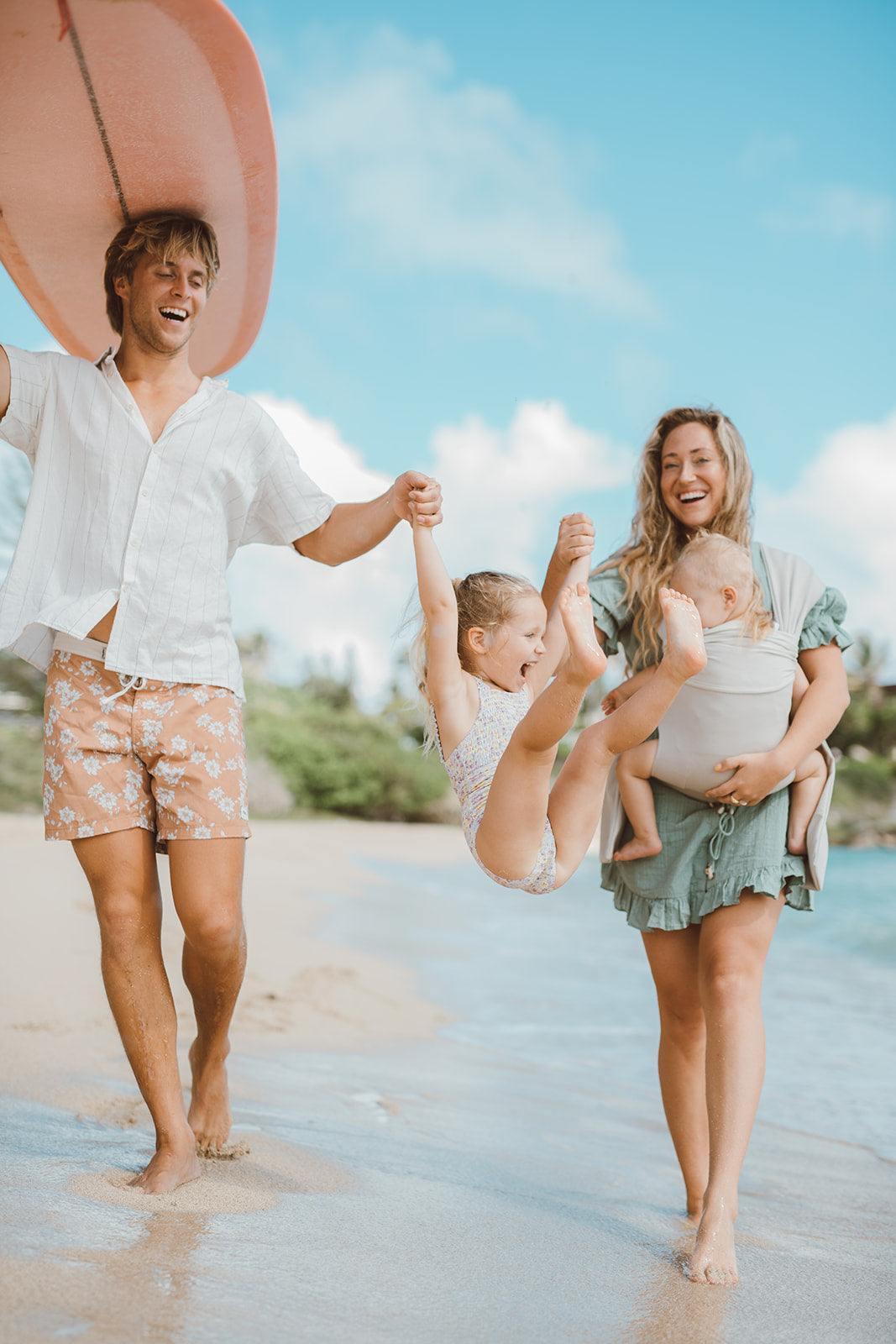 Female front carrying a baby in a Simple Wrap, on the beach with family.