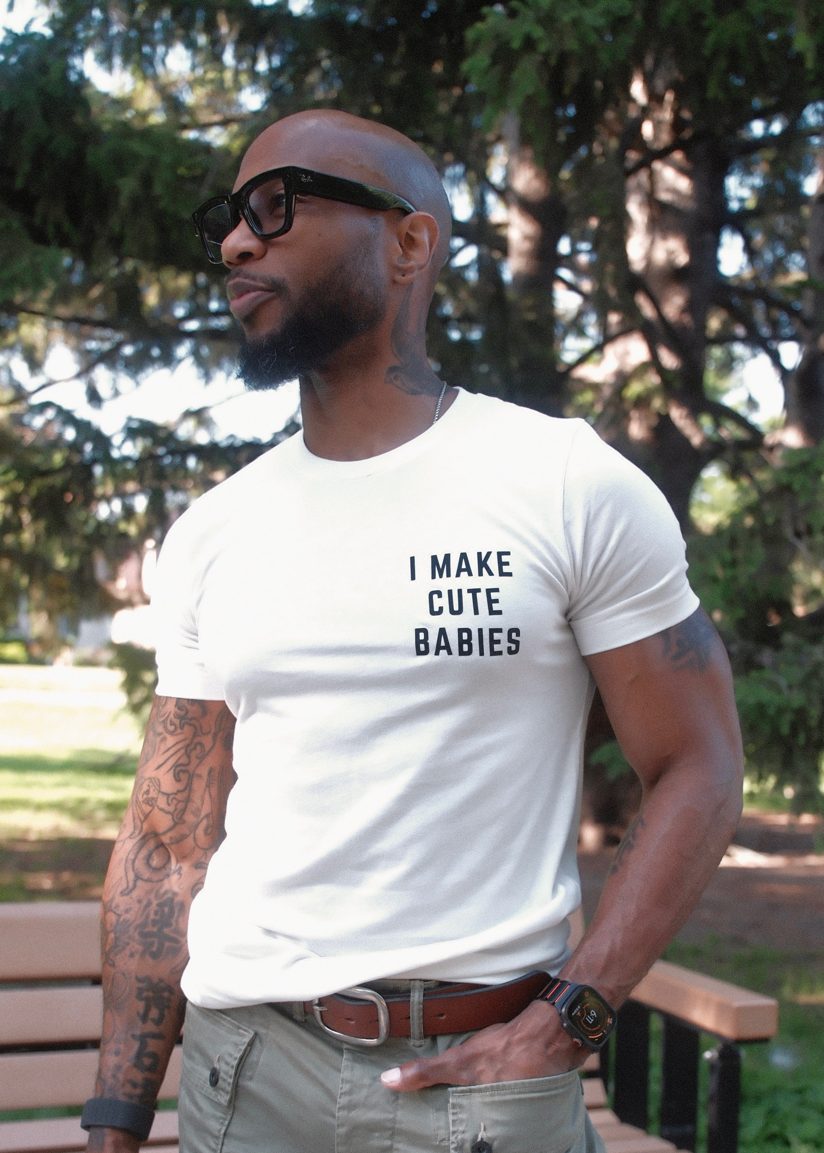 Man wearing a white t-shirt with 'I MAKE CUTE BABIES' text in black on the upper left chest of the shirt. 