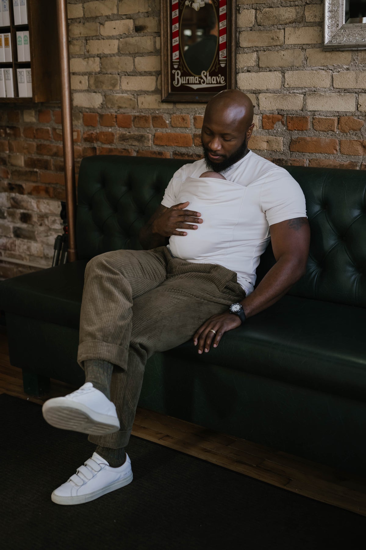 Male wearing a newborn in a Natural Dad Shirt, sitting on a couch.