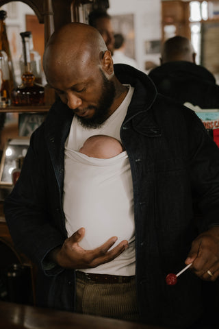 Male supporting a newborn in a Natural Dad shirt in a barbershop.