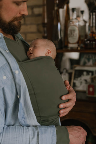 Male wearing a newborn in a Fern Dad Shirt.