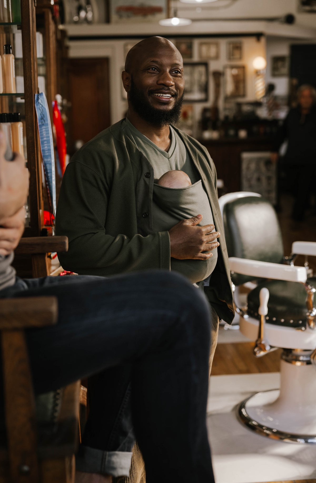 Male wearing a newborn in a Fern Dad Shirt, standing in a barbershop.