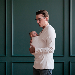 Side profile of a Dad wearing a newborn in a long sleeved Natural dad shirt with a green backdrop.