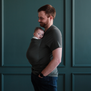 Side profile of a Dad wearing a newborn in a Fern dad shirt in front of a green backdrop.