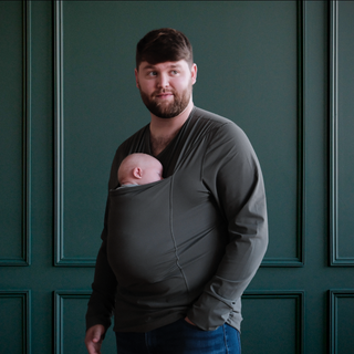 Dad wearing a newborn in a long sleeved fern dad shirt in front of a green backdrop.