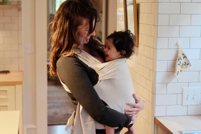 Mom smiling at the baby she's front carrying in a Fog Simple Wrap in the kitchen.