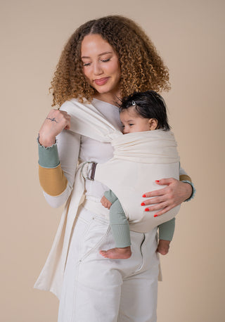 woman dressed in all white looking to her shoulder with a baby on her front in a cream simple wrap