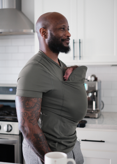 Dad in the kitchen with a newborn in the pouch of his Fern Dad Shirt.