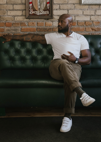 Dad wearing his newborn in the pouch of a natural Dad Shirt, while sitting on a couch.