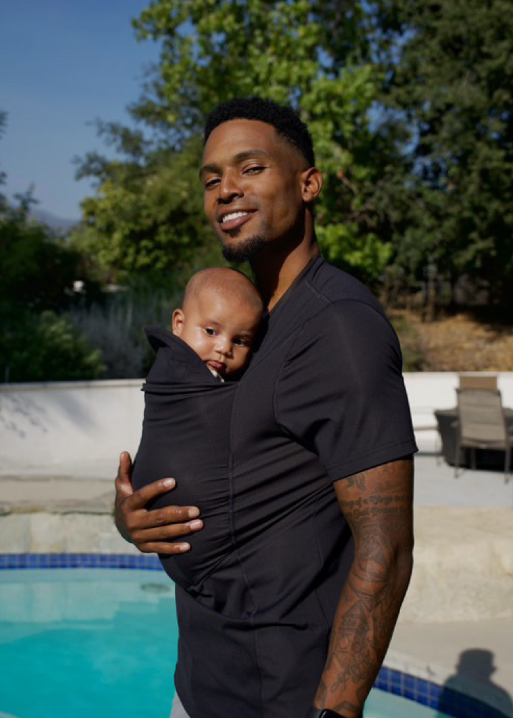 Dad wearing his baby in the pouch of his Black Dad shirt while poolside.