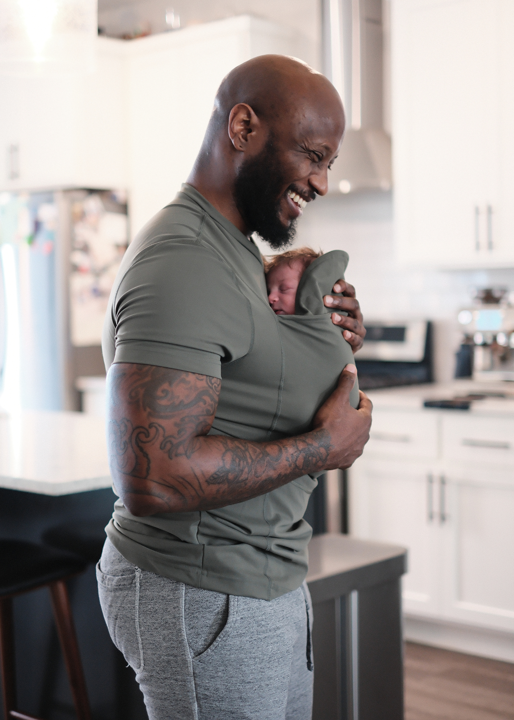 Dad smiles while snuggling the newborn in the pouch of his Fern Dad Shirt.