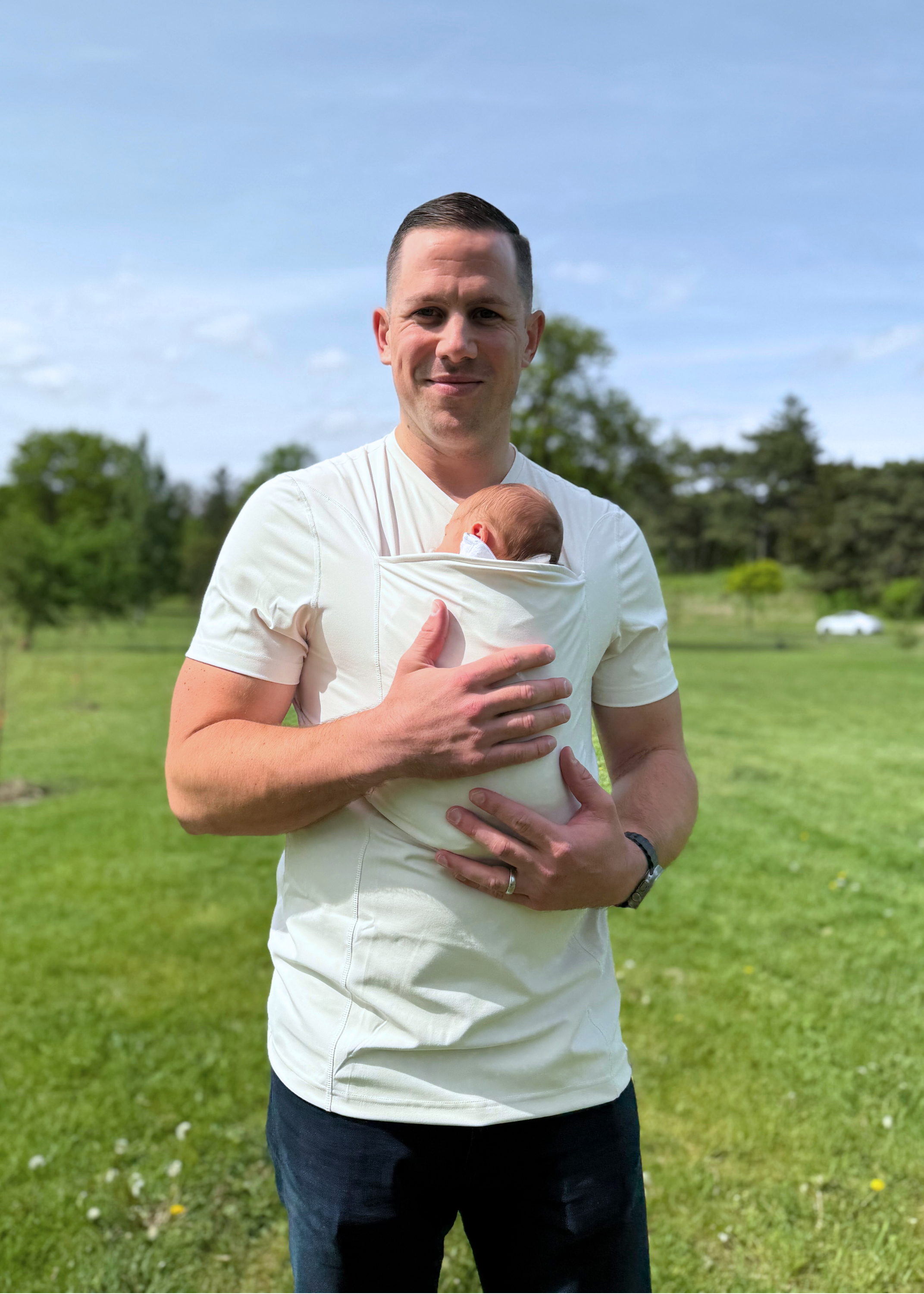 Dad snuggling the newborn in the pouch of his Natural Dad Shirt at the park.