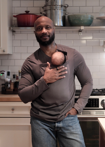 Dad wearing his newborn in a long sleeve Gray Dad Shirt in the kitchen. 