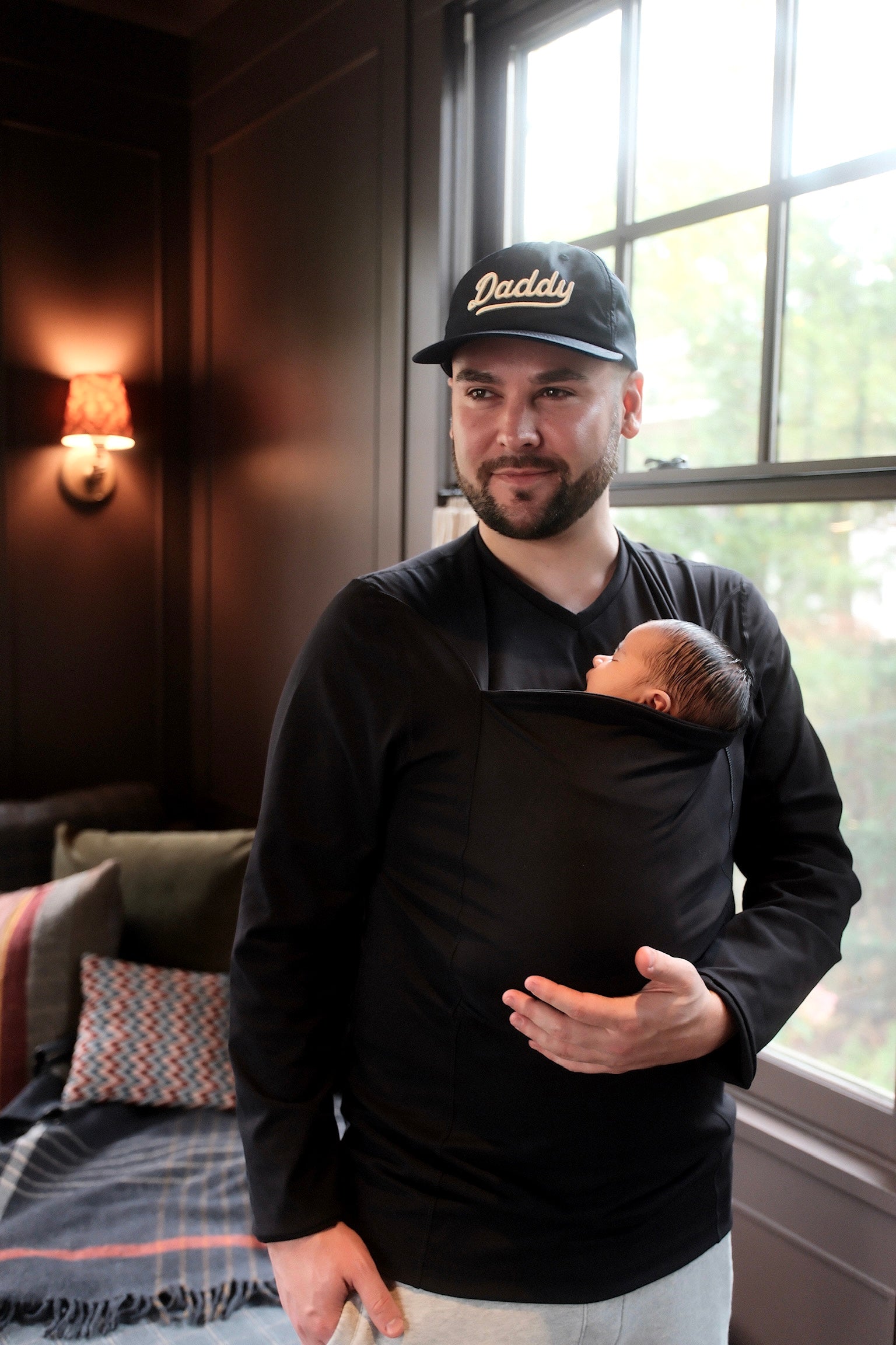 Dad wearing his newborn in the pouch of his Black Long Sleeve Dad Shirt and sporting a Daddy cap.