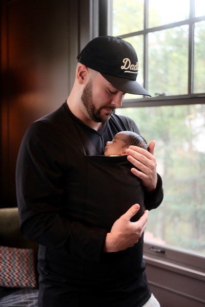 Dad wearing his sleeping newborn in his Black long sleeve Dad Shirt sporting a Daddy cap.
