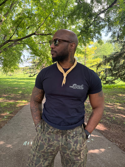 Model wearing navy "The Dad" shirt at a park.