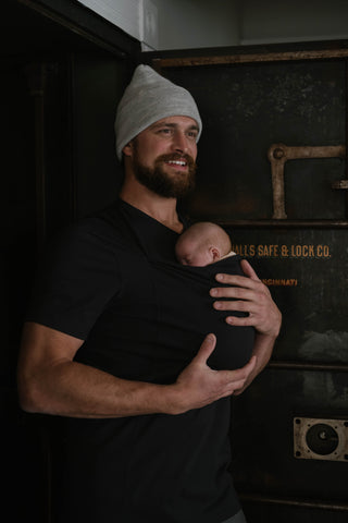 Male wearing a newborn in a black Dad Shirt.