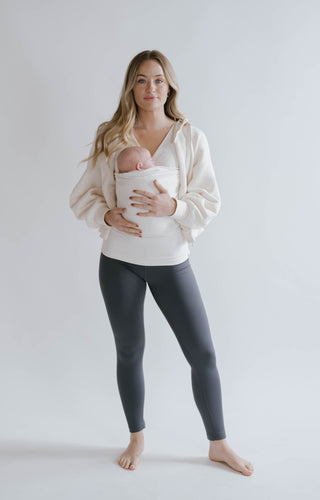 Full body view of a female wearing a newborn in a Natural Soothe Shirt.