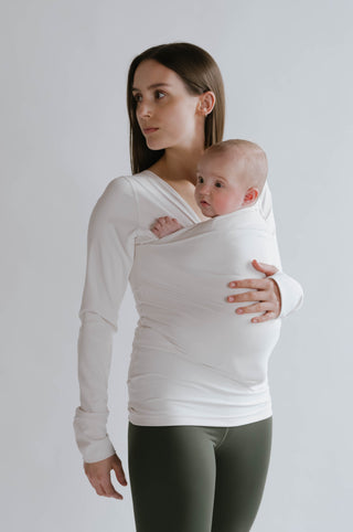 Angled view of a female wearing a newborn in a Natural long sleeve Soothe Shirt.