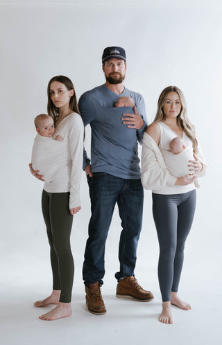 2 females wearing newborns in tank top and long sleeve sleeve Soothe Shirts on either side of a male wearing a newborn in a brook Dad Shirt.