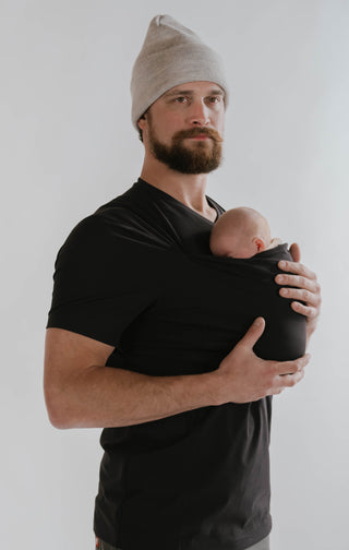 Male wearing a newborn in a black Dad Shirt.