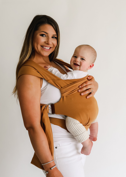 Mom front carrying her baby in a Camel Simple Wrap, both are smiling at the camera.
