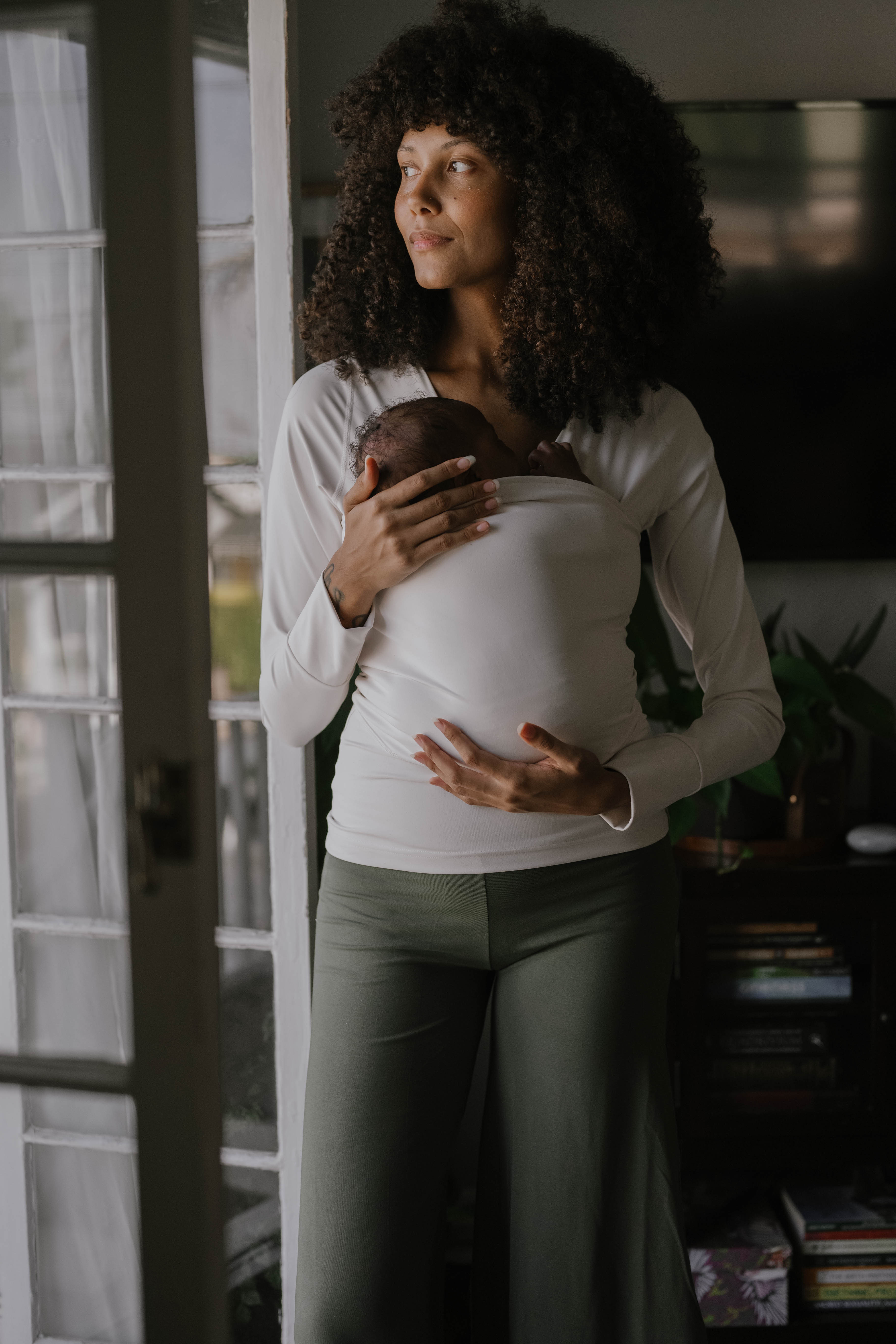 Female in front of opened doors wearing a newborn in a Natural long sleeve Soothe Shirt.