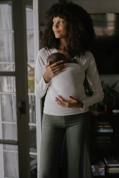Female in front of opened doors wearing a newborn in a Natural long sleeve Soothe Shirt.