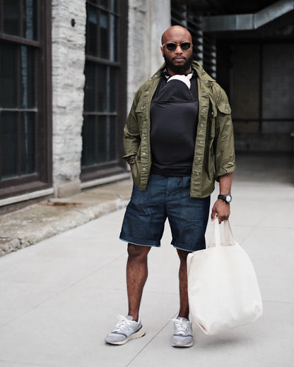 Dad wearing a newborn in a black Dad shirt, in front of a building.