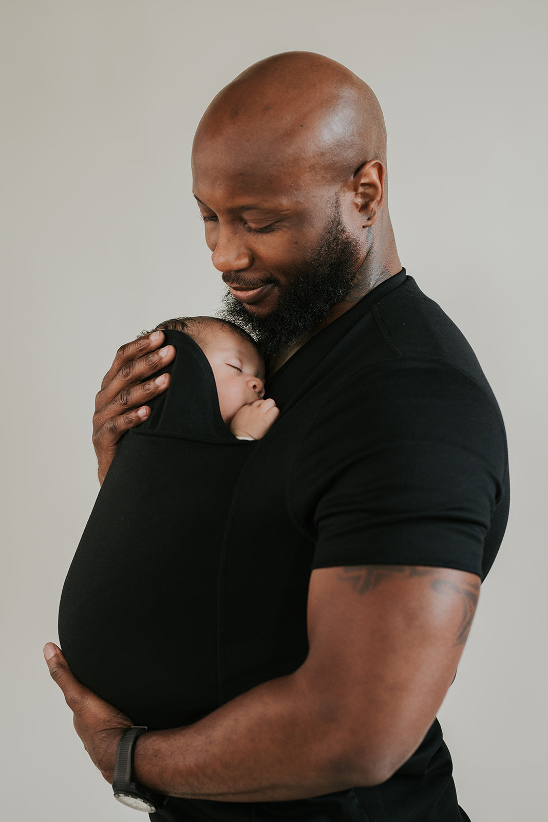 Dad looking at the newborn he's wearing in a black Dad Shirt