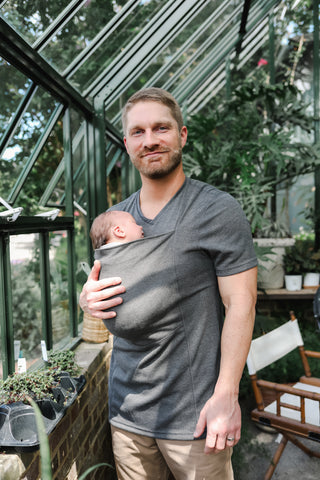 Dad wearing newborn in a Dad Shirt inside a greenhouse.